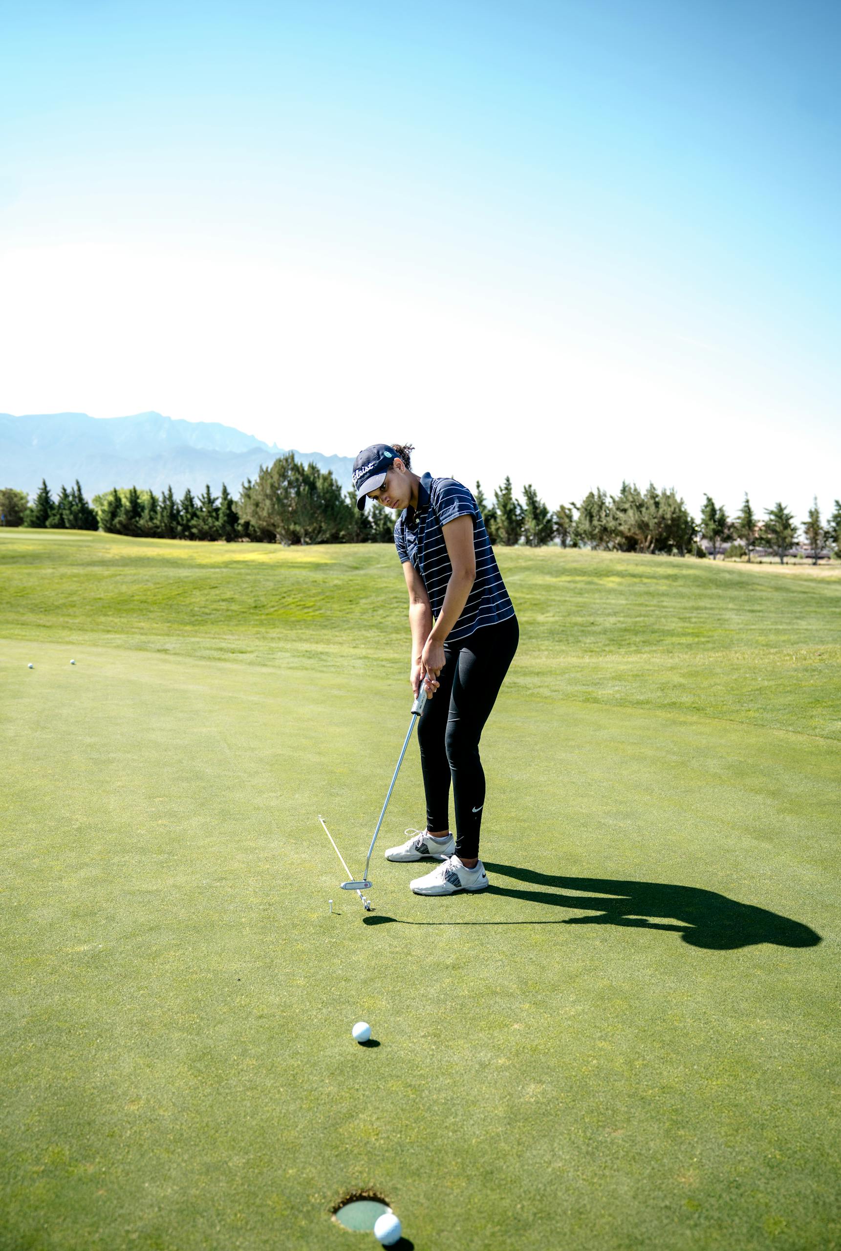 A woman golfer concentrates while putting on a sunny day at a golf course.